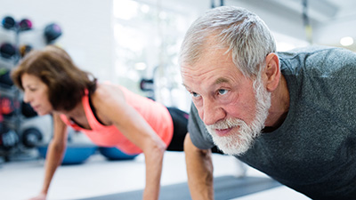 Senior couple in gym working out, doing push ups